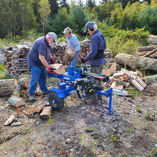 Several people using a wood splitter to make firewood